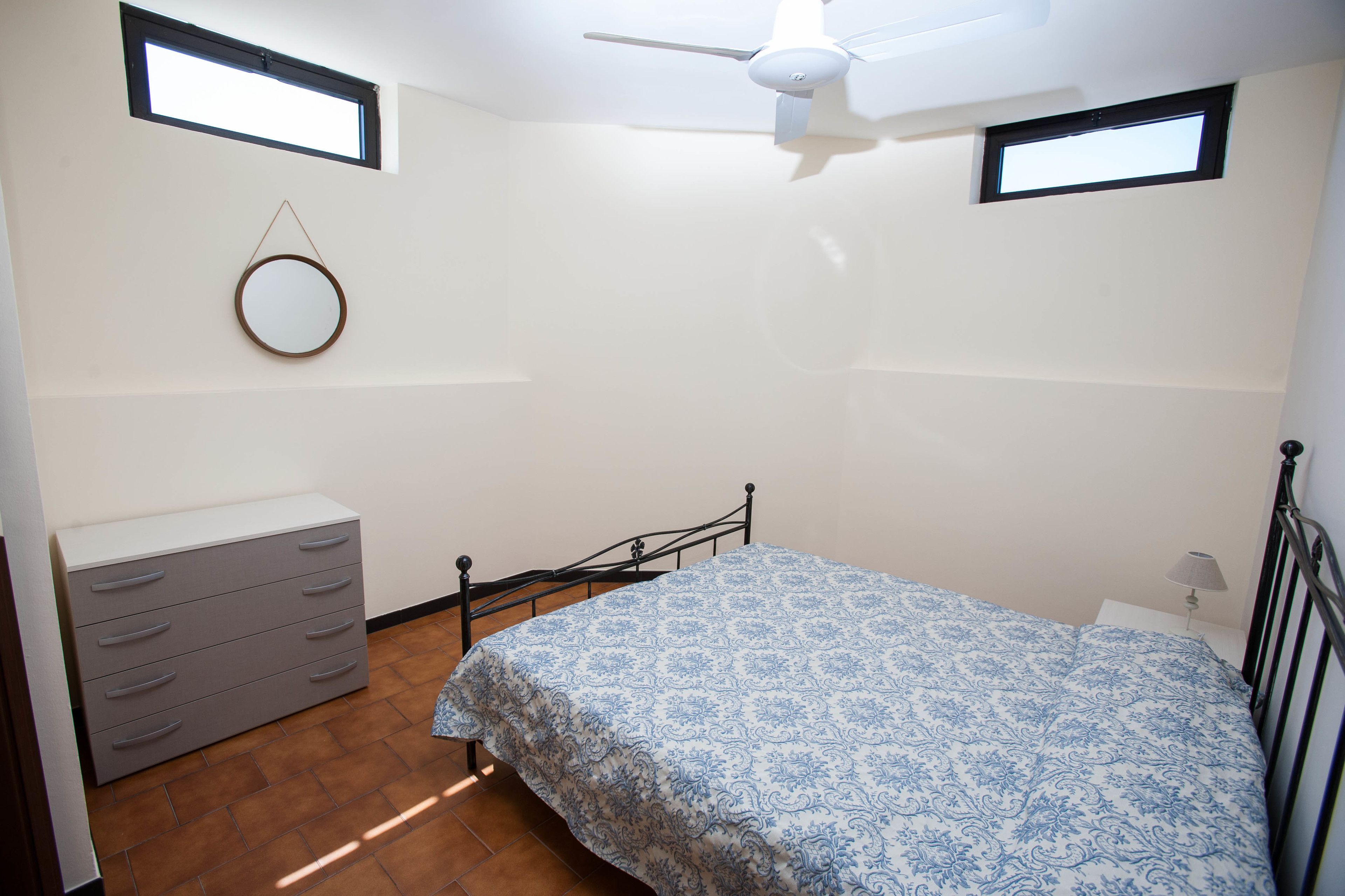 Une chambre à coucher comprenant un lit, une commode, un ventilateur de plafond et deux fenêtres.