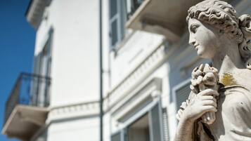 Una statua raffigura una figura con un grappolo d'uva, posta di fronte a un edificio dalle caratteristiche architettoniche classiche.