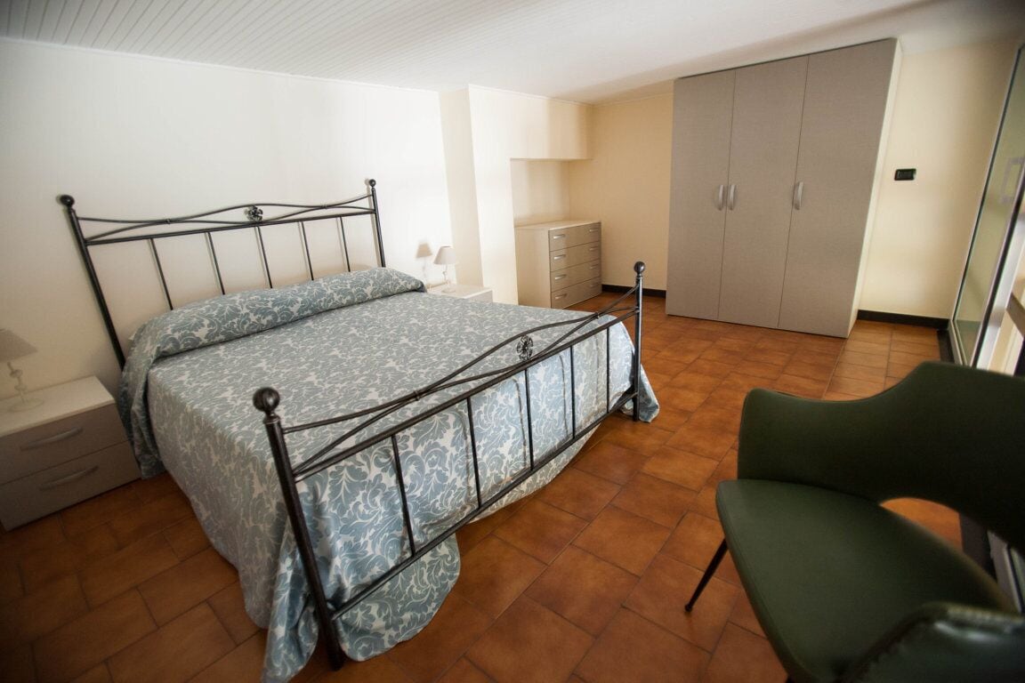 Ein Schlafzimmer mit einem Metallbettgestell, einem grünen Sessel, einem Kleiderschrank und einer Heizung.