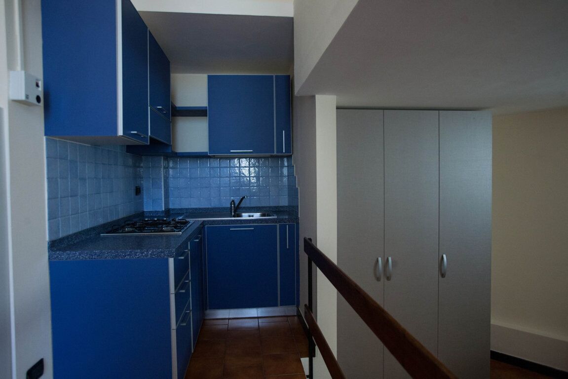 A narrow kitchen with blue cabinets, a stove, and a sink.