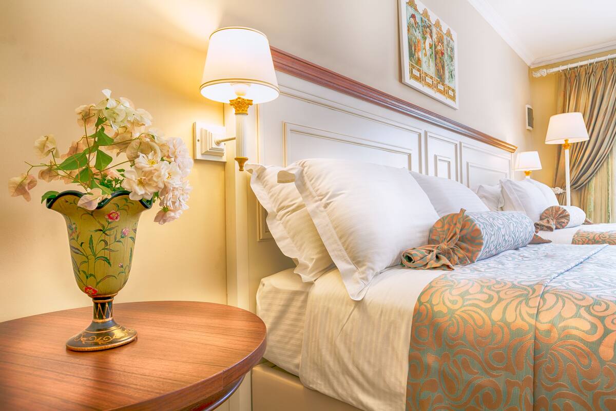 Ein Hotelzimmer mit einem Bett, einem Nachttisch mit Blumenvase und zwei Nachttischlampen.