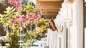 A woman in a white dress standing by a white building with a balcony, surrounded by lush greenery and flowering plants. - Dalyan Resort SPA - Boutique Class (Ortaca)