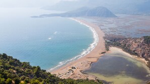 Vista aérea de una zona costera con playa, aguas azules cristalinas y montañas al fondo.