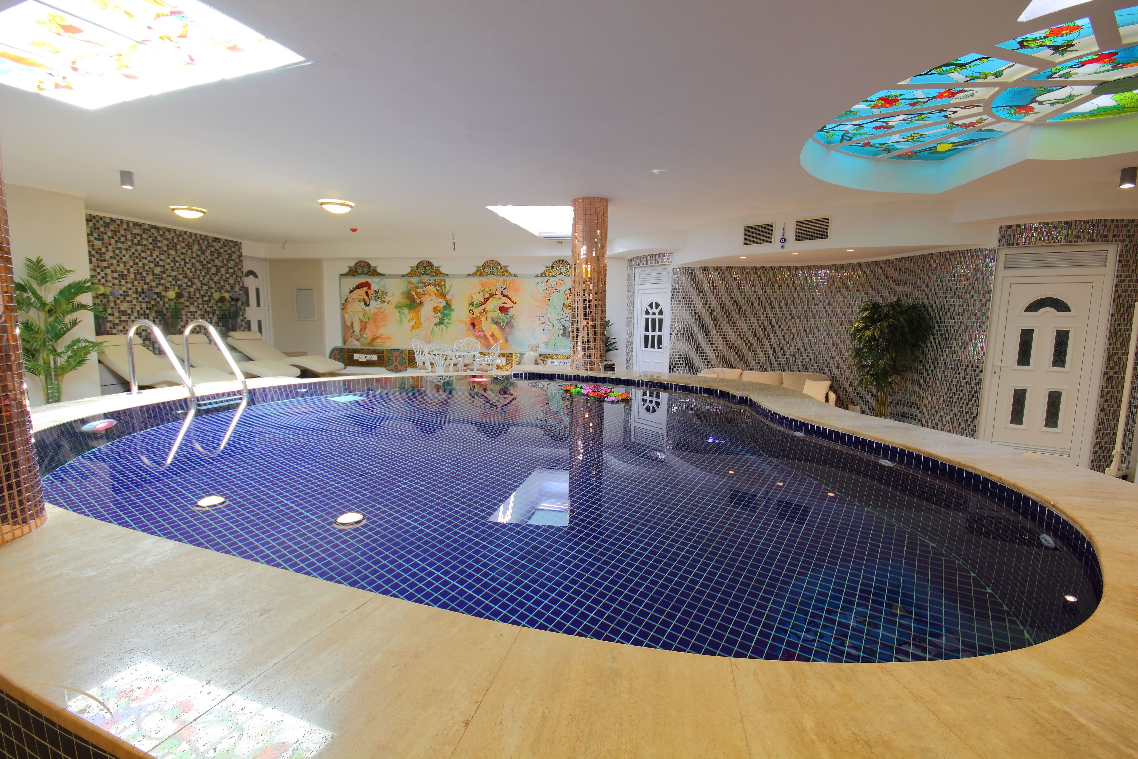 An indoor swimming pool with a tiled floor, a ladder, and a mural on the back wall.
