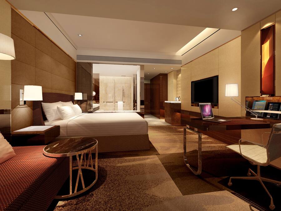 Una habitación de hotel moderna con una cama grande, un escritorio con computadora, televisor y un área de descanso con una silla y una mesita.