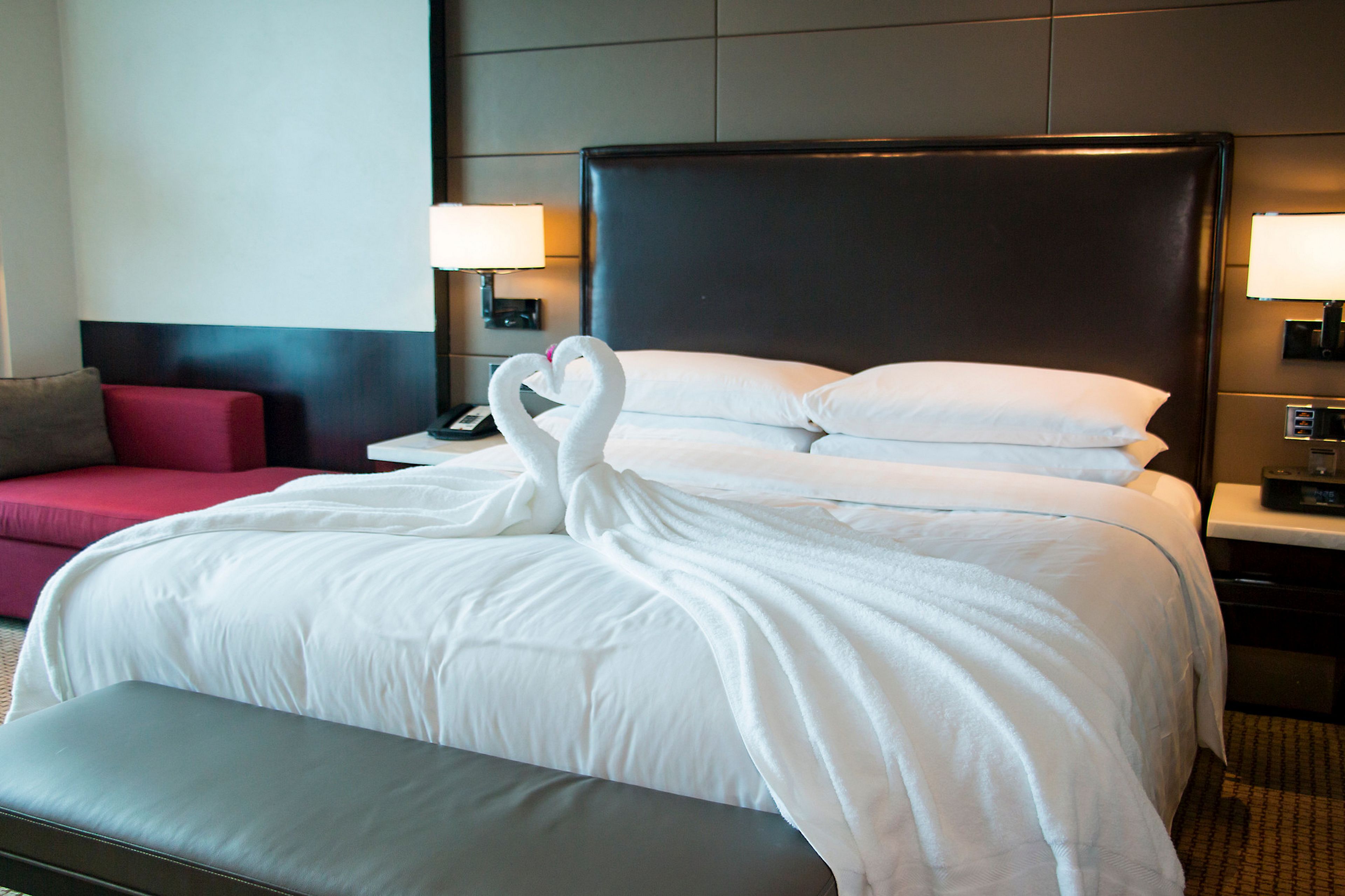 Una habitación de hotel con una cama grande, dos lámparas de noche, un sofá rojo y una mesita con un teléfono.
