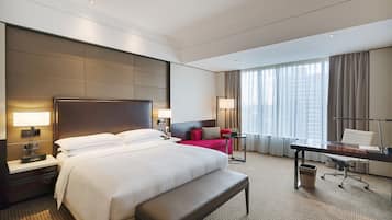 Una habitación de hotel con una cama grande, un escritorio con silla, un sofá rojo y un ventanal con cortinas.