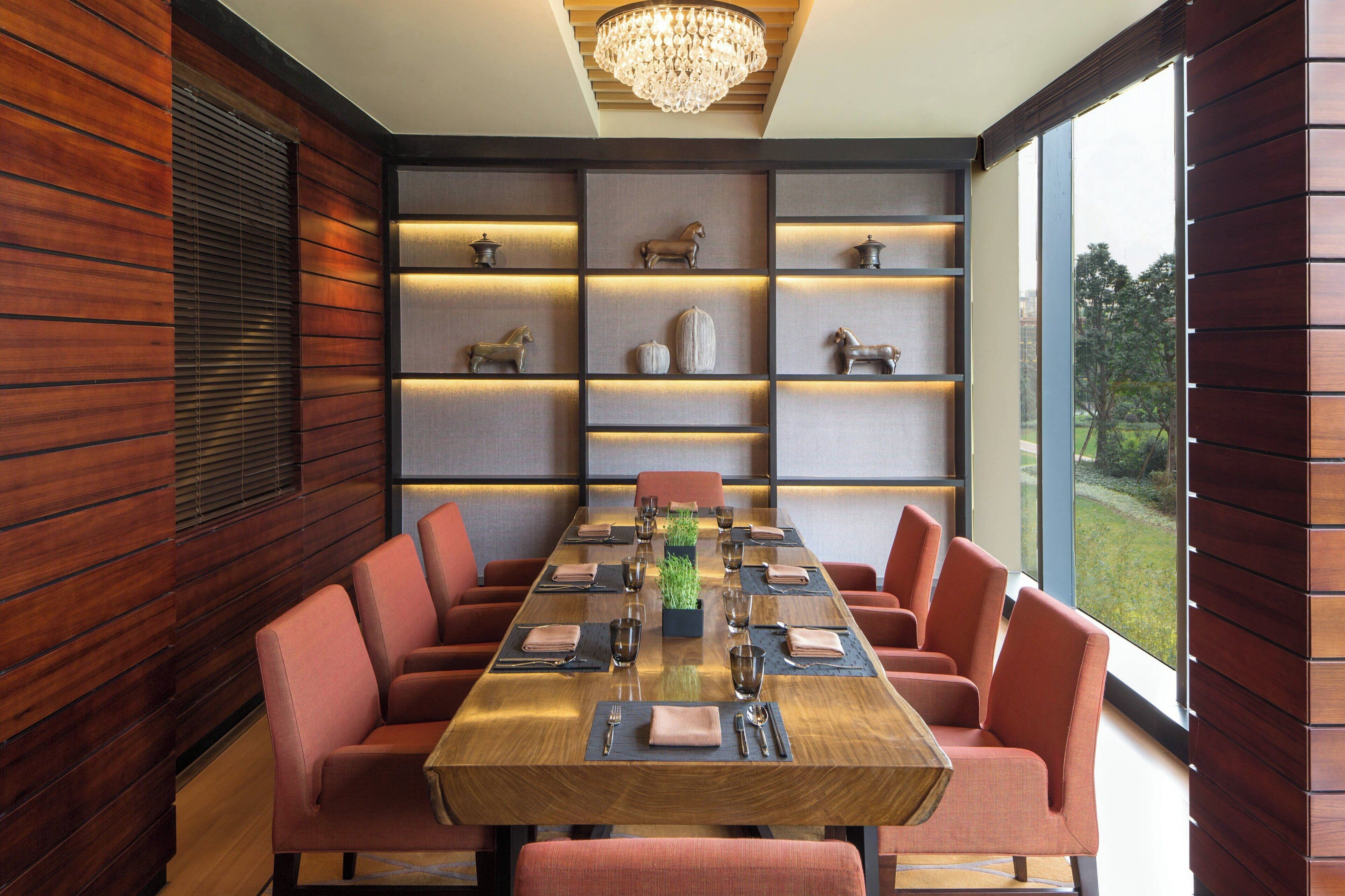 Une salle à manger moderne avec une table en bois dressée pour huit personnes, entourée de chaises à revêtement rouge.