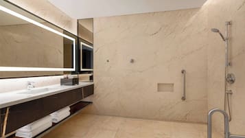 Un baño moderno con pared de mármol, un espejo grande, un lavabo, una ducha con cabezal de ducha manual y un perchero para toallas.