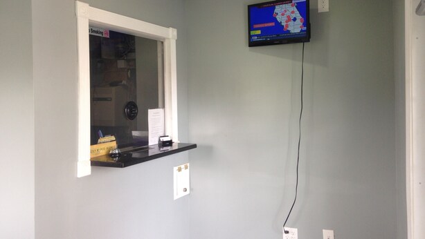 A room with a mounted TV displaying a weather map, a window with a smoke detector, and a small shelf with items. - Ole English Inn (Tuscaloosa)
