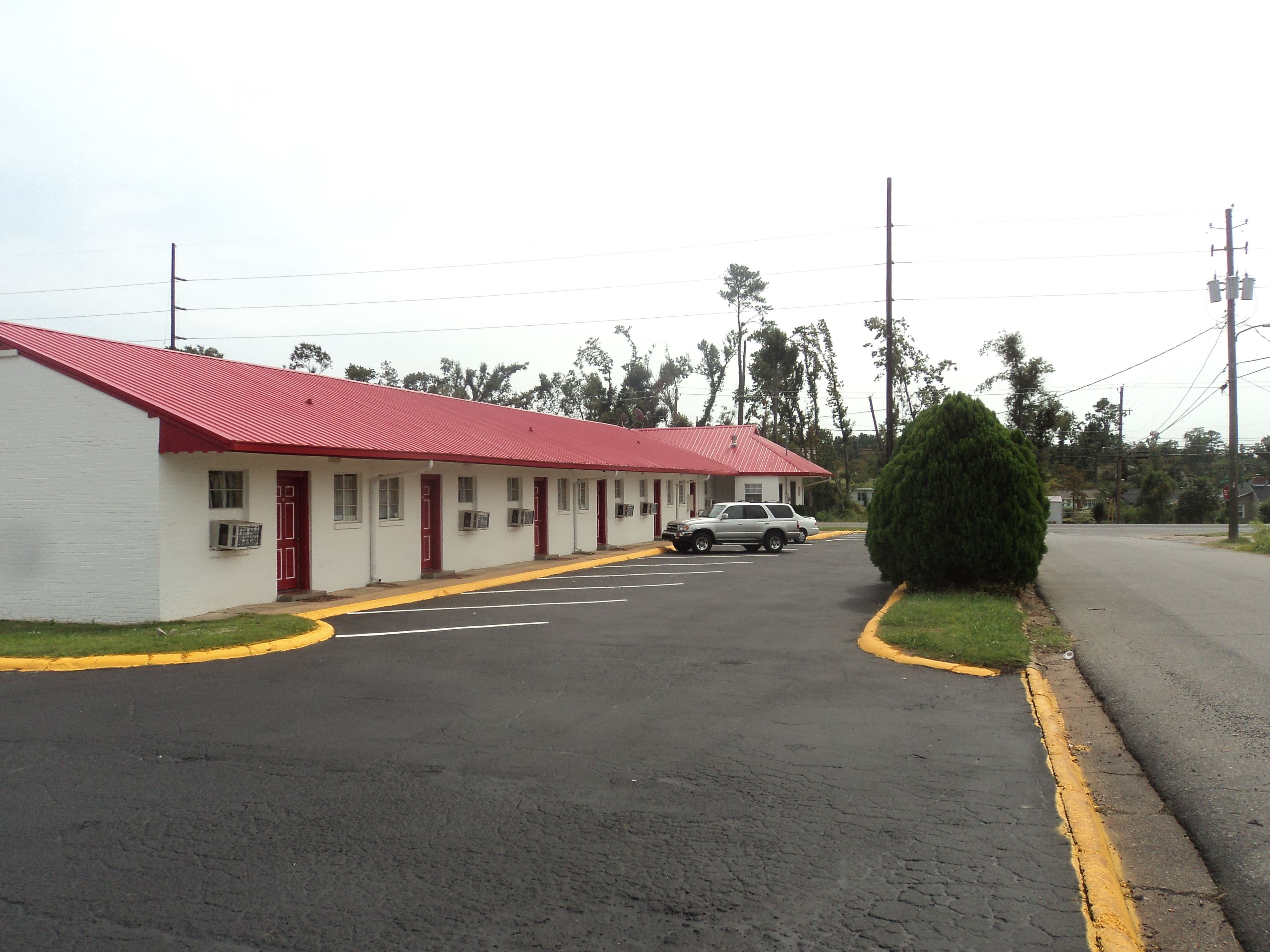 A motel with a red roof and white walls, a parking lot, and a single vehicle parked in front.