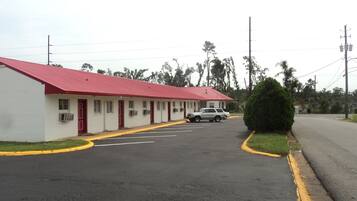 A motel with a red roof and white walls, a parking lot, and a single vehicle parked in front.