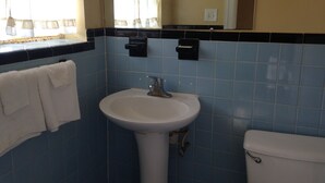 A bathroom with a white sink, a toilet, and a window with curtains. - Ole English Inn (Tuscaloosa)