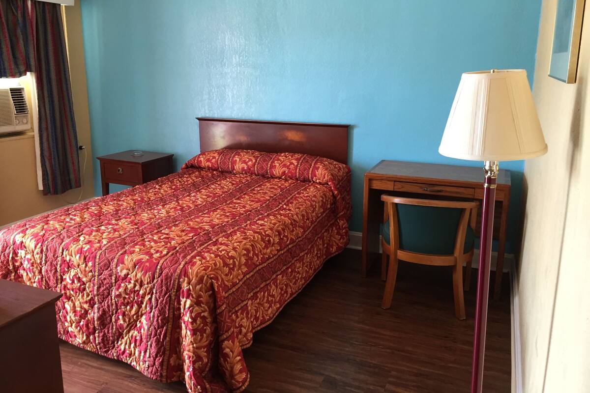 Een hotelkamer met een bed, nachtkastje, lamp en een raam met gordijnen.