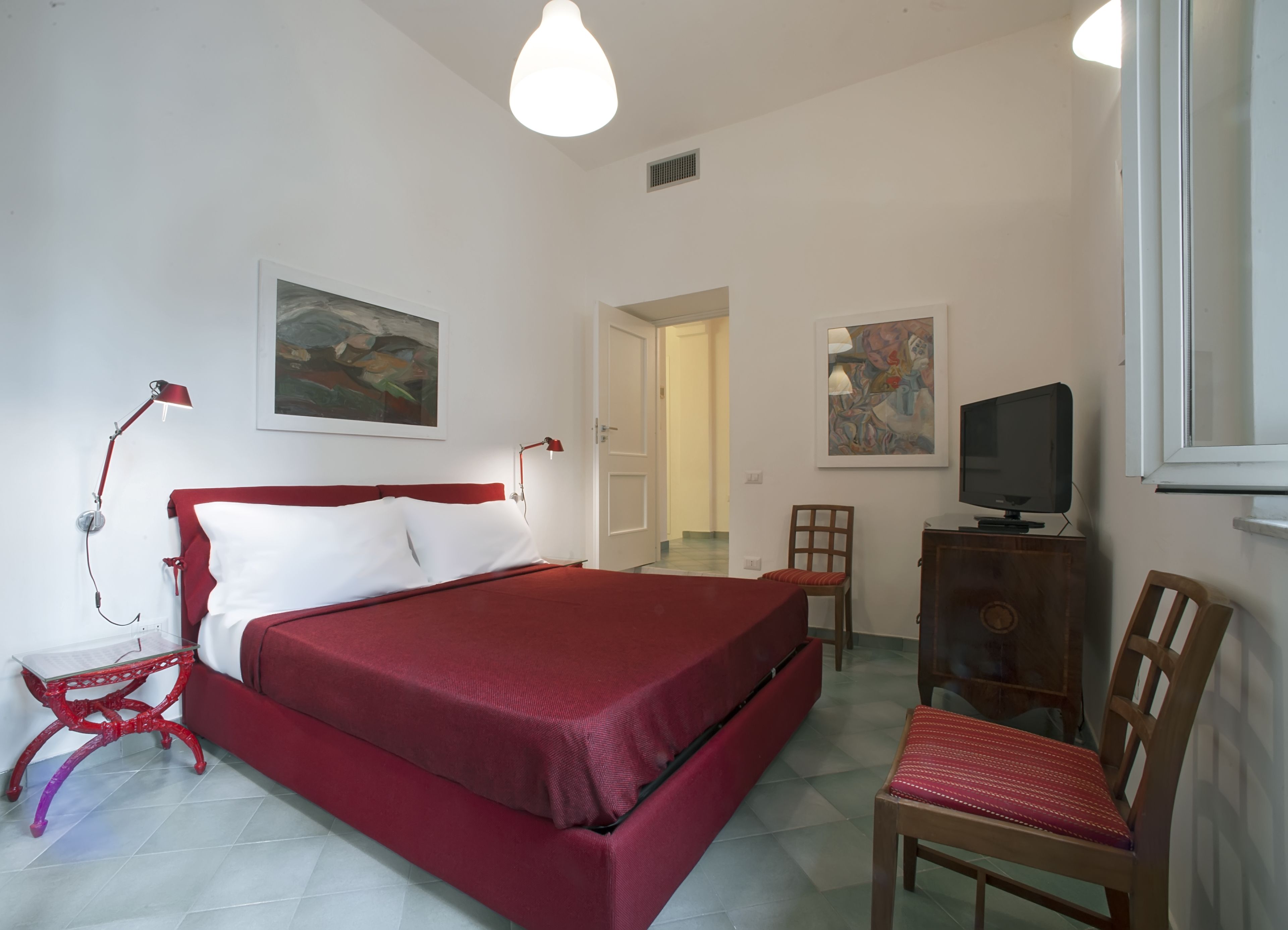 Ein Schlafzimmer mit einem roten Bett, einem Schreibtisch mit Fernseher und zwei Stühlen.