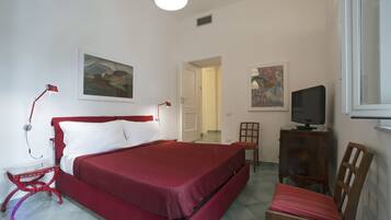 Ein Schlafzimmer mit einem roten Bett, einem Schreibtisch mit Fernseher und zwei Stühlen.