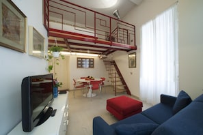 A living room with a TV, sofa, dining table, chairs, and a staircase. - Casa Vittoria (Naples)