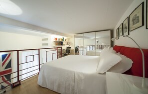 A bedroom with a large bed, a desk, and a chair. There is a bookshelf with books and decorative items. A flag is visible in the corner. - Casa Vittoria (Naples)