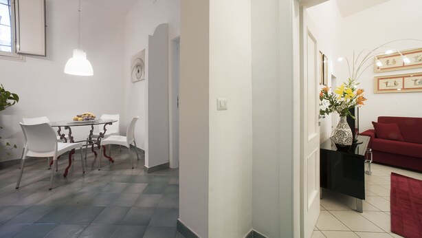 A modern living room with a red sofa, a dining area with a glass table and white chairs, and a hallway with a red rug. - Casa Vittoria (Naples)