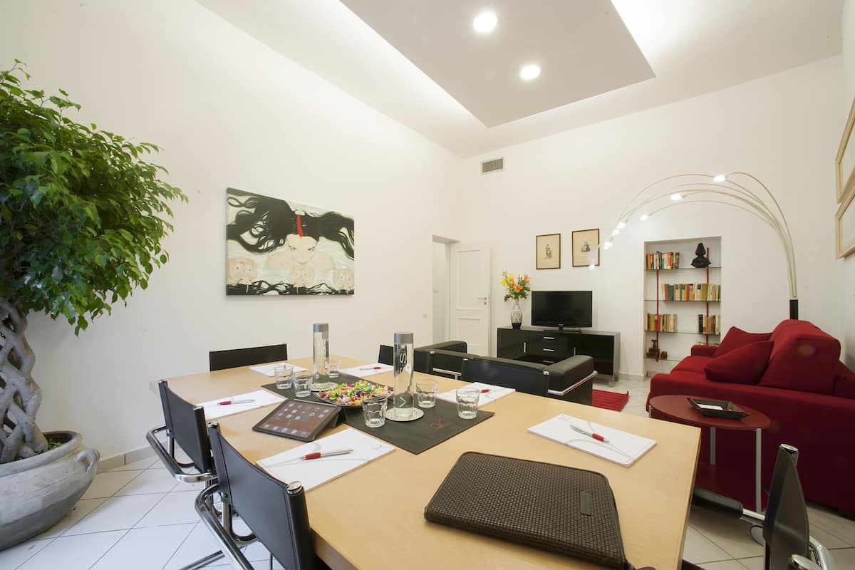 Un salon moderne comprenant un coin repas, un canapé rouge, un téléviseur et une bibliothèque.