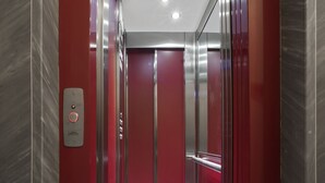 An elevator interior with metallic walls, a red door, and a control panel with a button. - Casa Vittoria (Naples)