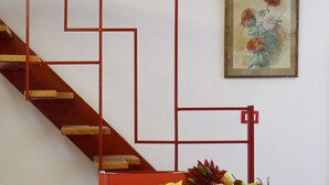 A staircase with a geometric railing design, a fruit bowl on a table, and a framed floral painting on the wall. - Casa Vittoria (Naples)