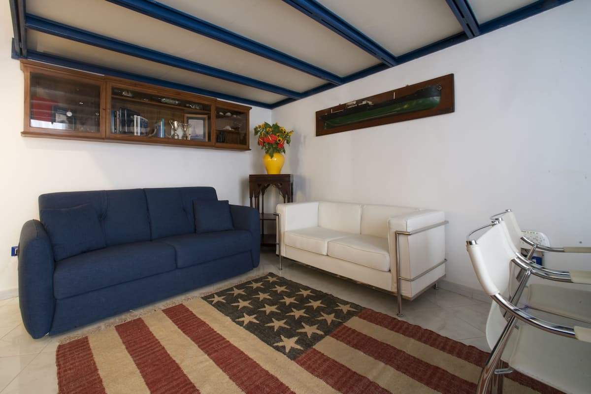 Un salon avec un canapé bleu, un canapé blanc et une petite table sur laquelle est posé un vase de fleurs.