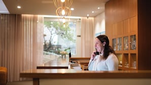 A reception area with a wooden counter, a telephone, and a view of a garden through large windows. - Adelaide Hotel (Terras de Bouro)
