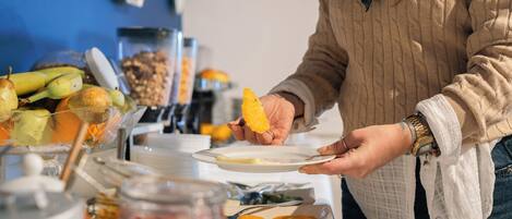 A buffet table with various food items and a person serving orange slices.