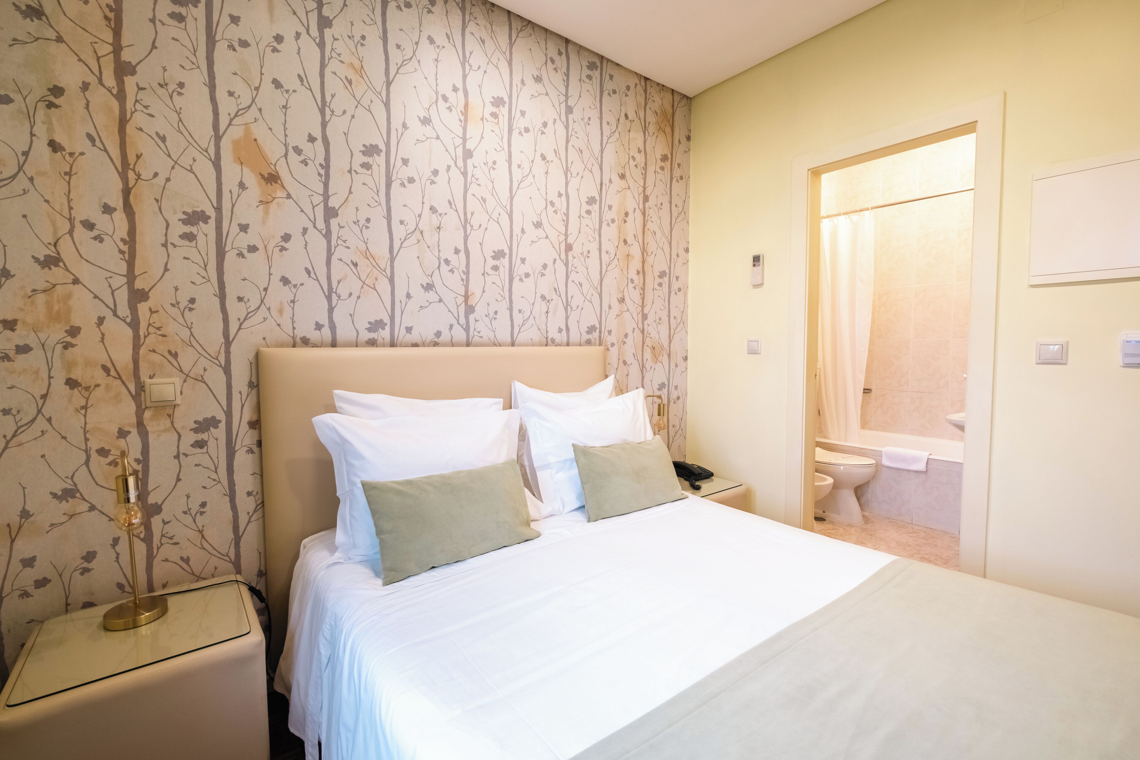 A hotel room with a bed, nightstand, and a bathroom visible through an open door.