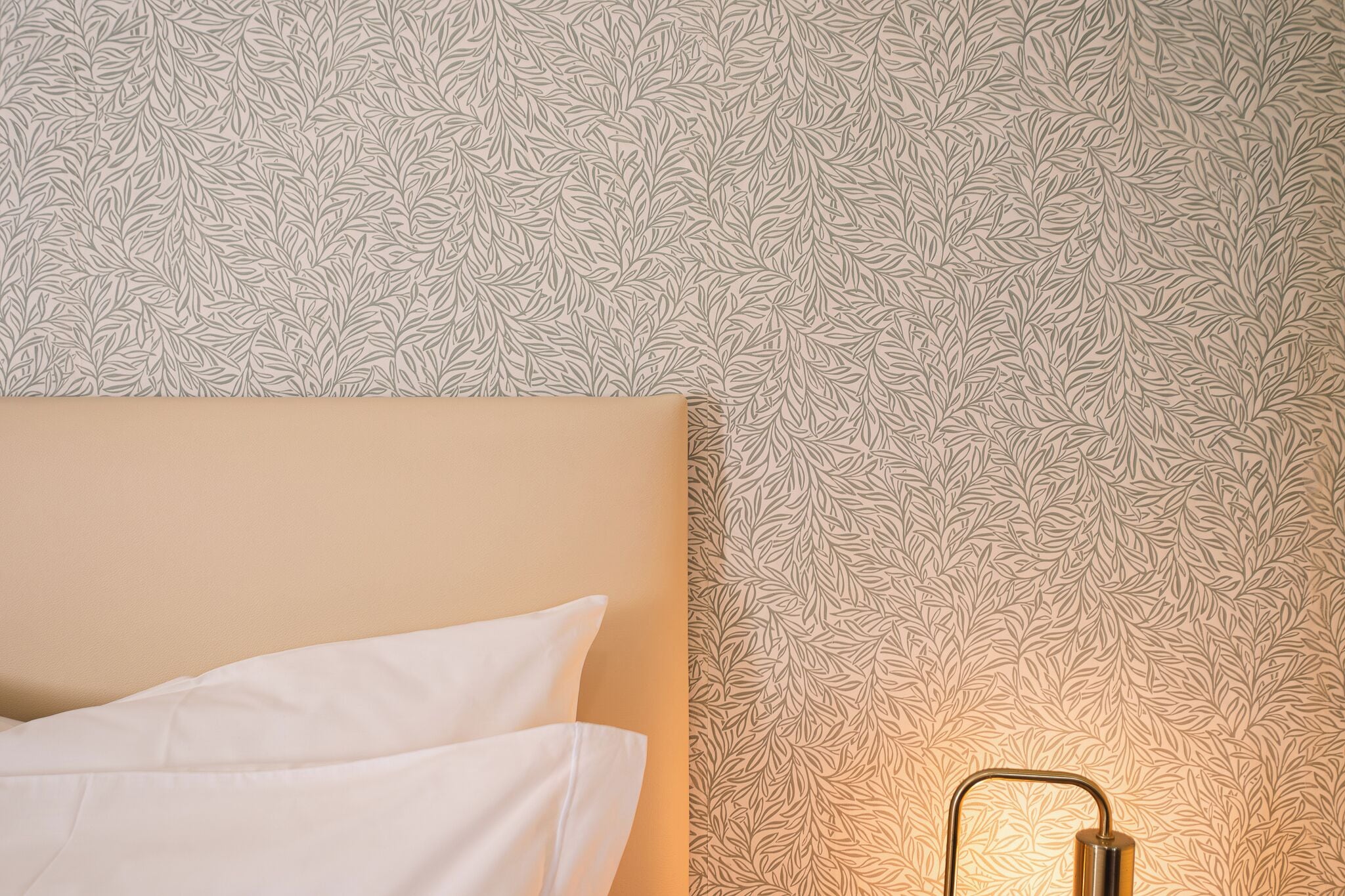 Un lit avec une literie blanche, un papier peint à motifs et un luminaire fixé au mur.