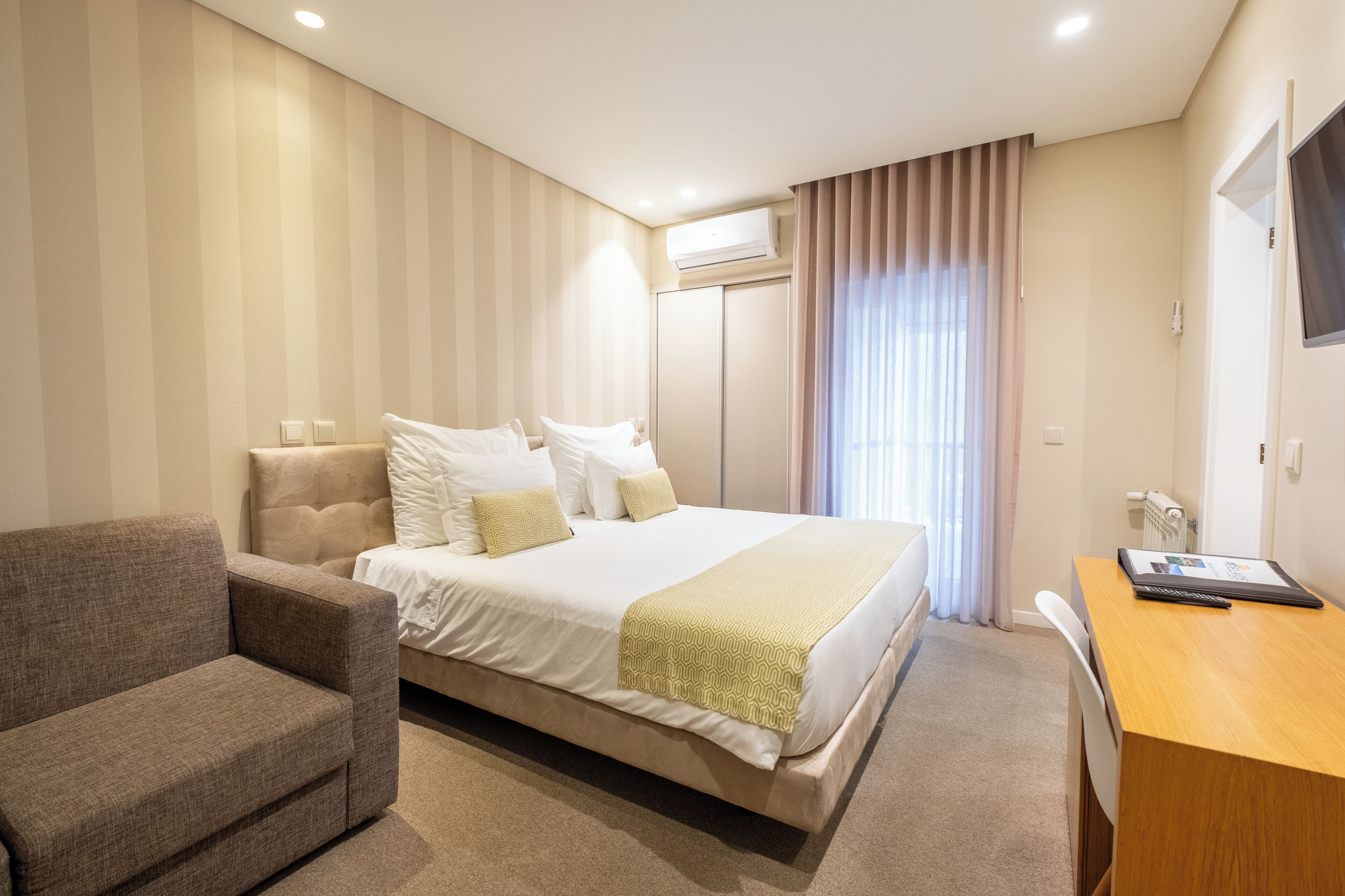 A hotel room with a bed, a sofa, a desk, and an air conditioning unit.