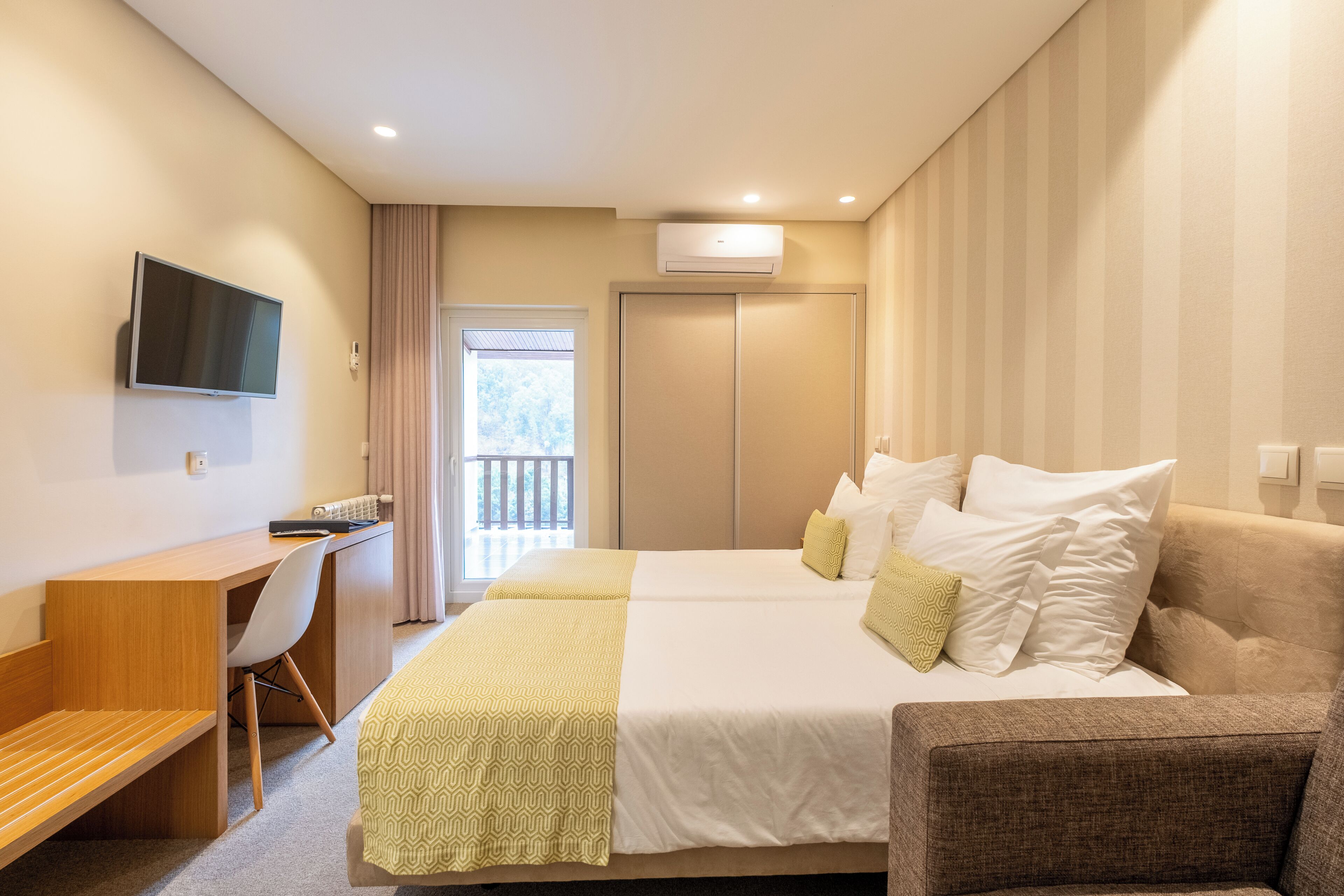 Une chambre d’hôtel avec un lit, un bureau, une chaise, une télévision et un balcon.