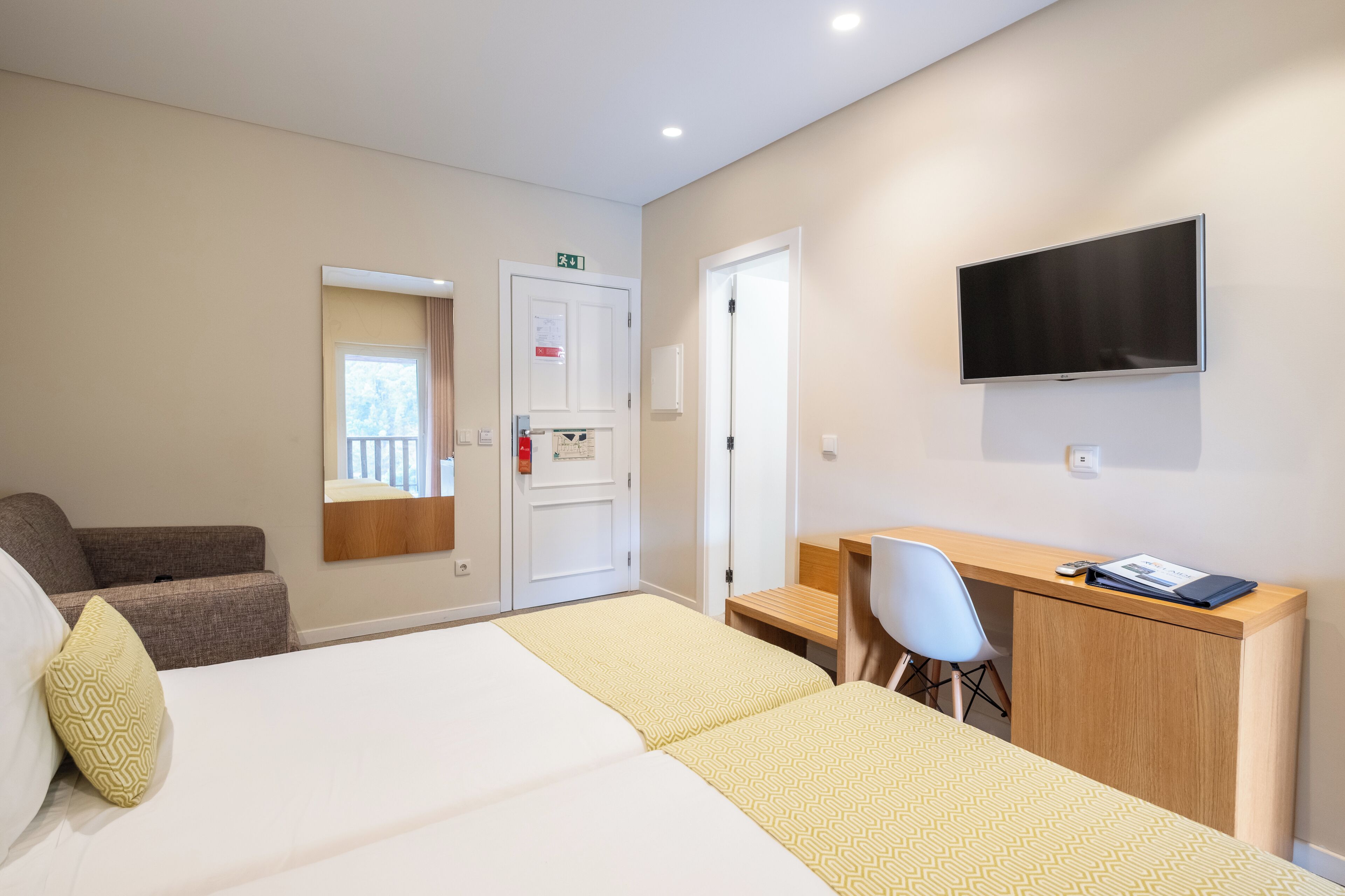 Une chambre d’hôtel équipée d’un lit, d’un bureau, d’une chaise, d’une télévision et d’une porte signalant une issue de secours.
