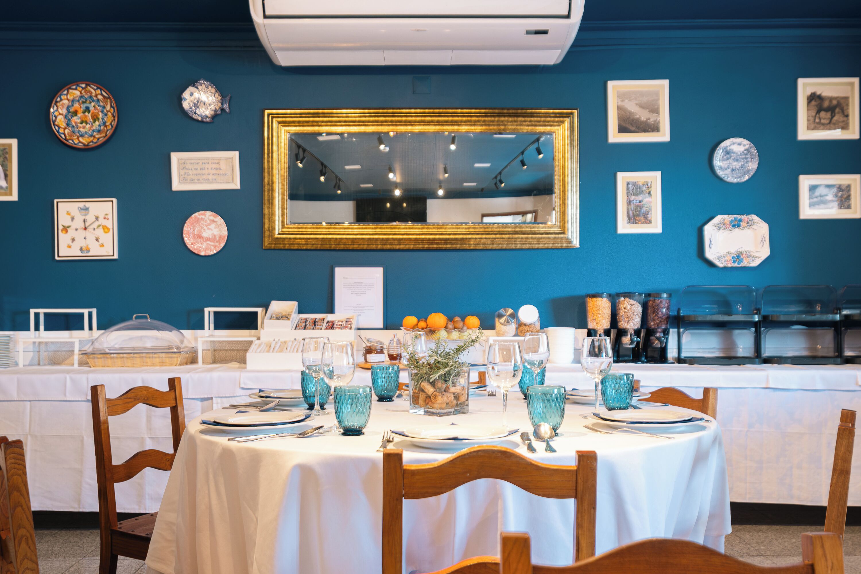 A dining area with tables set for service, a large mirror on the wall, and various decorative plates and vases.