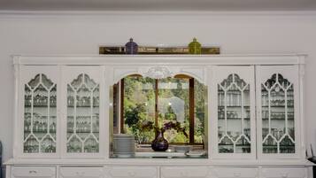 A white cabinet with glass doors, a vase with flowers, and a view of greenery outside.
