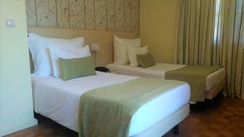 Habitación de hotel con dos camas, una mesita de noche, una lámpara y una ventana con cortinas.