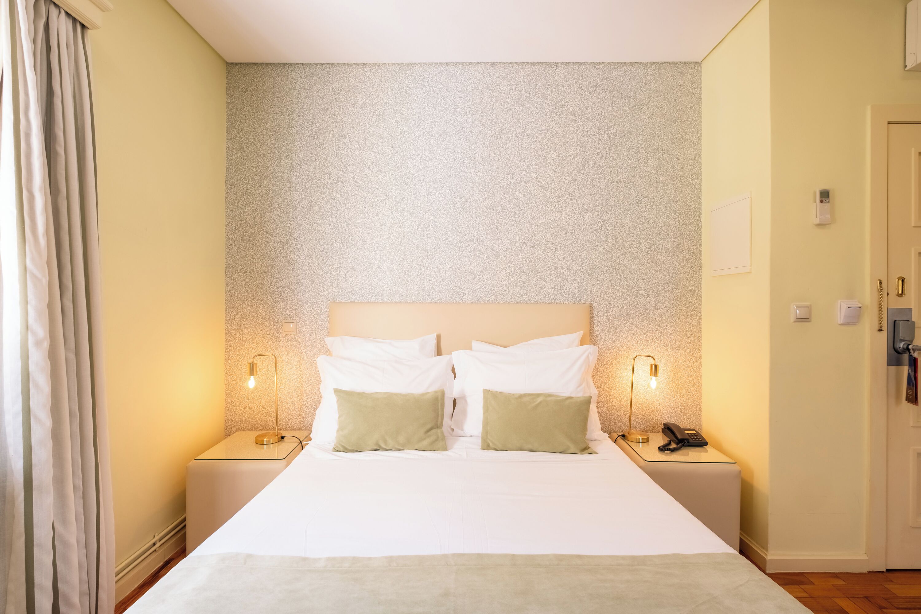 Une chambre d’hôtel avec un grand lit, deux lampes de chevet, un téléphone et une porte à clé.