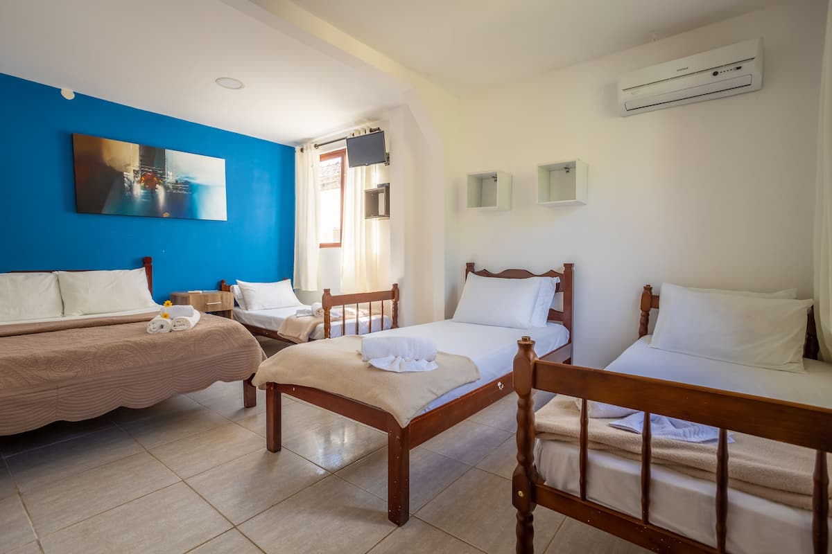 A hotel room with two single beds, a TV, an air conditioner, and a painting on the wall.