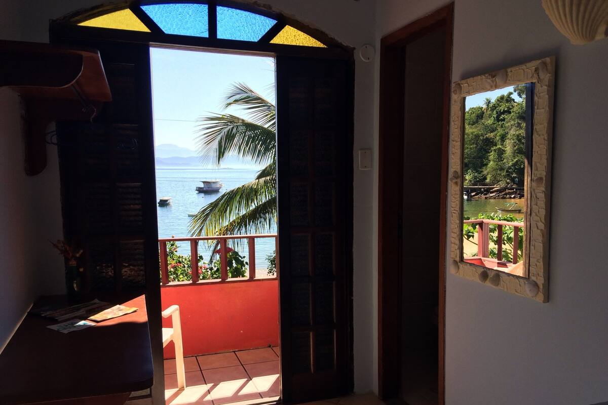 An open door leading to a balcony with a view of the sea and boats.