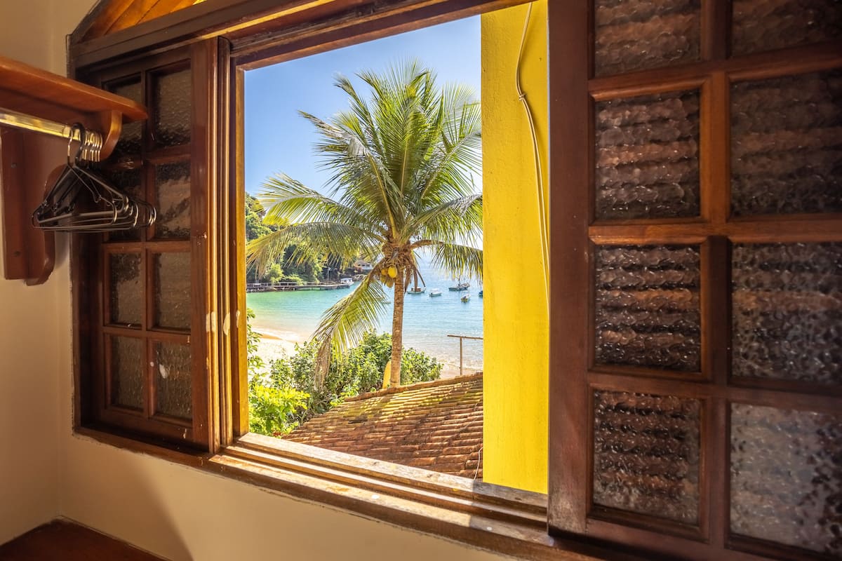 A window with a view of a beach, palm tree, and boats.