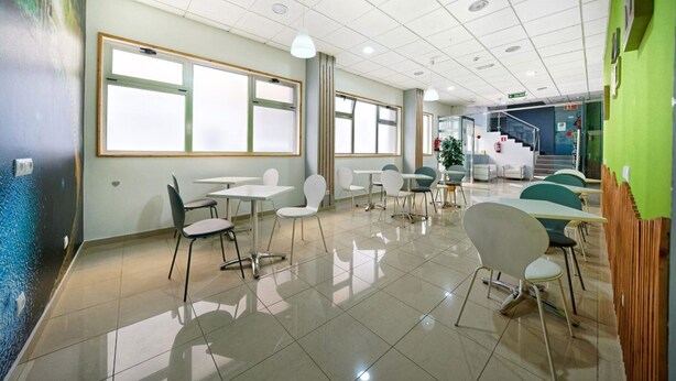 A modern dining area with tables and chairs, large windows, and a staircase in the background. - Boji (Las Palmas de Gran Canaria)
