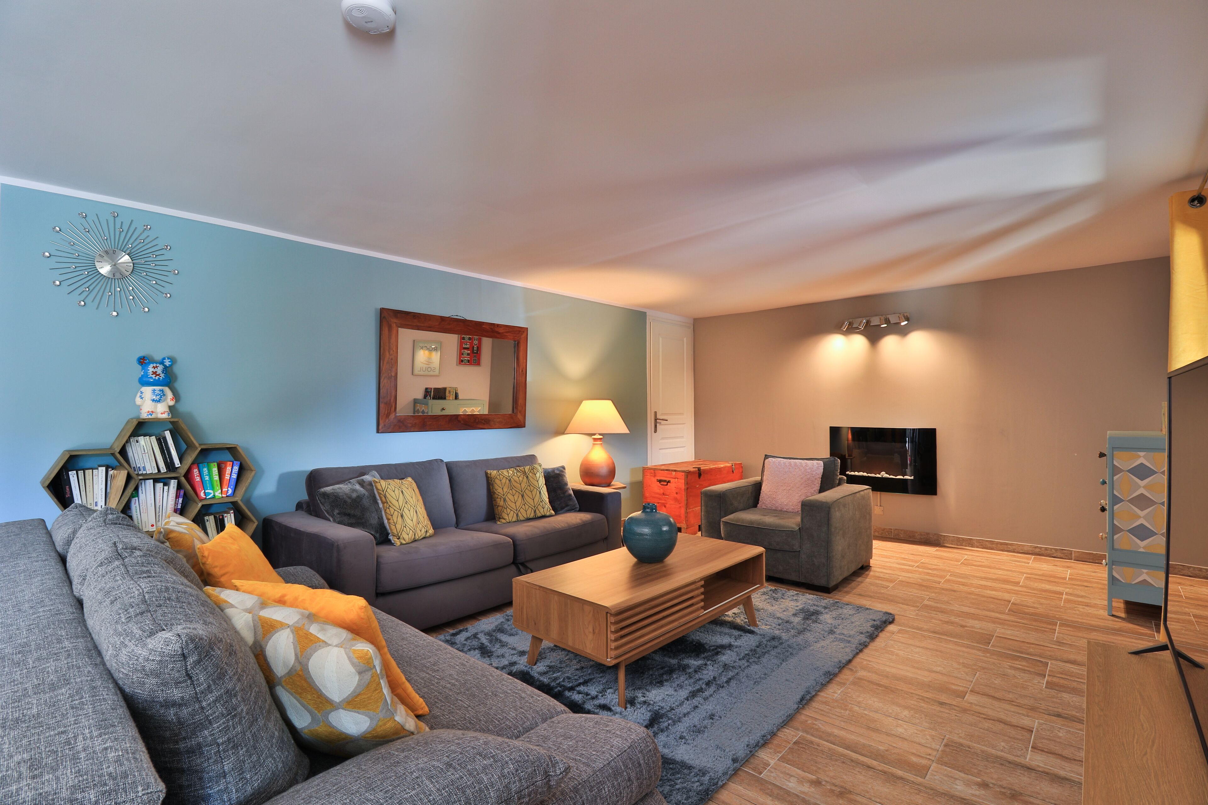 A modern living room with a grey sofa, a wooden coffee table, and a bookshelf.