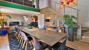 A spacious dining area with a long table and multiple chairs, a staircase with a metal railing, and a large world map on the wall. - Lalpen Roc (Caille)