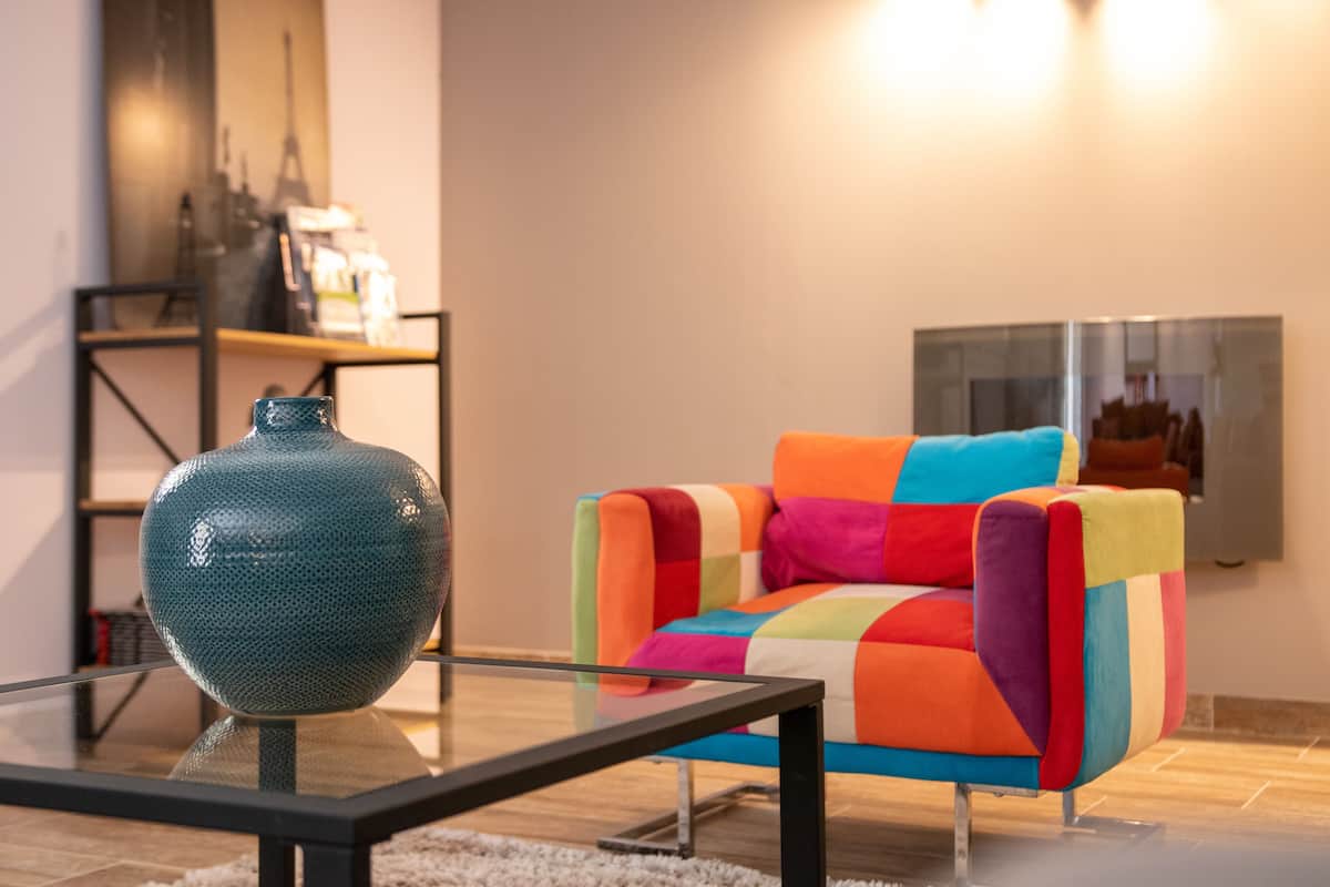 Una sala moderna con un sillón colorido, una mesa de centro de vidrio y un jarrón decorativo.