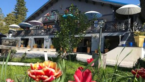 A building with a balcony and outdoor umbrellas, surrounded by greenery and tulips. - Lalpen Roc (Caille)