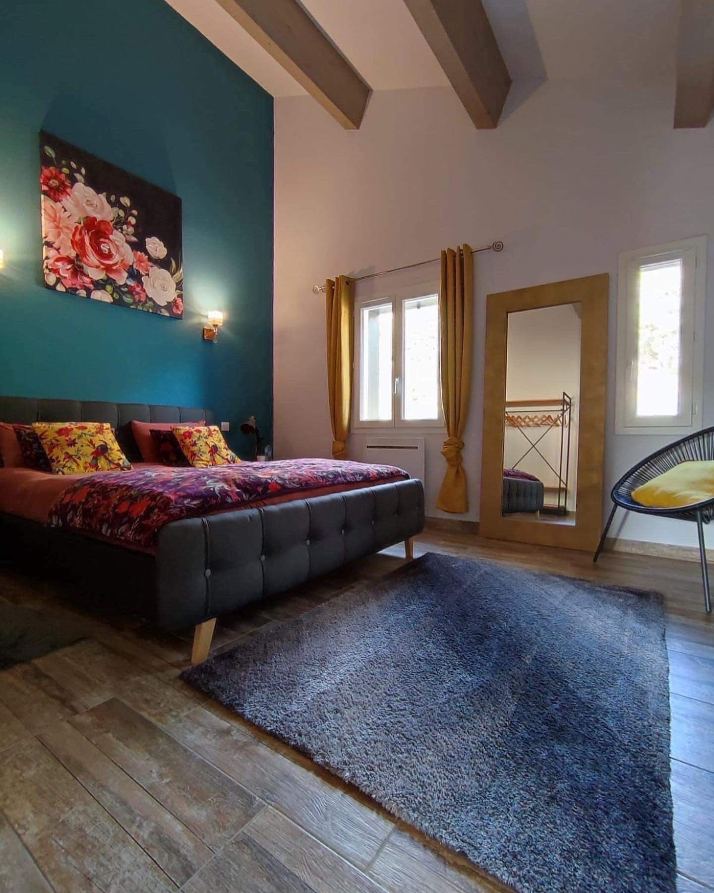 Een slaapkamer met een bed, een groot bloemschilderij, een raam met gordijnen en uitzicht op een balkon.