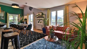 A modern living room with a sofa, dining table, chairs, and a large window. - Lalpen Roc (Caille)
