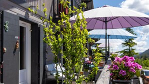 A wooden bench with a planter of pink flowers, a purple umbrella, and a building entrance. - Lalpen Roc (Caille)