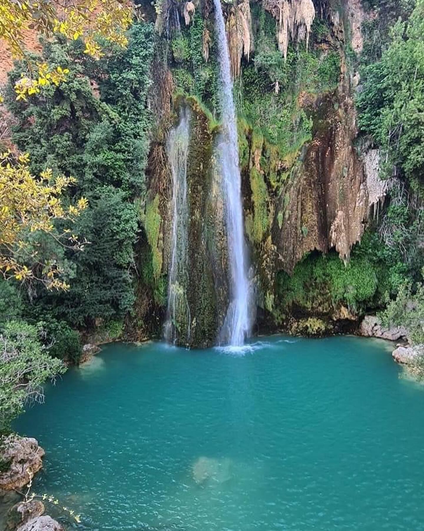 Een waterval stort neer in een helderblauw poel, omringd door weelderige begroeiing.